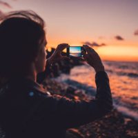 Woman on beach holiday taking photos with smartphone on sunset
